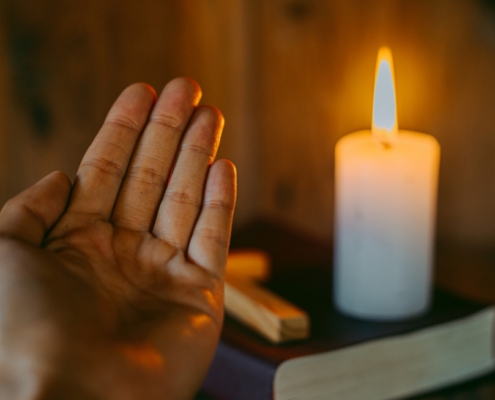 A candle burns a light on top of the bible beside a cross. Use the light of resurrection to spread God's love.