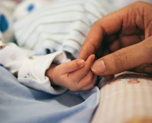 person holding baby's index finger illustrating the dignity of the human person